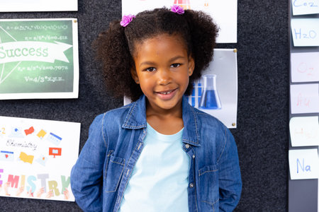 Portrait of african american schoolgirl in school classroom with chemistry posters in background....