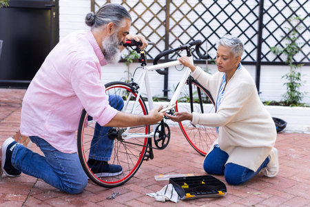 Repairing bicycle together, senior couple working with tools in backyard. Biking, maintenance, seniors, teamwork, outdoor, lifestyleの写真素材