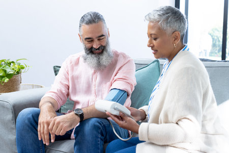 Checking blood pressure, woman using monitor on man sitting on couch. Healthcare, wellness, monitoring, checkup, hypertension, preventionの写真素材