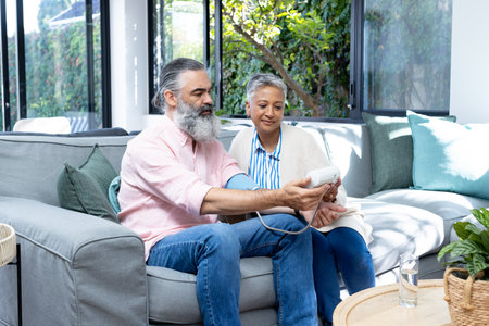 Senior couple checking blood pressure with monitor while sitting on couch. Healthcare, seniors,...