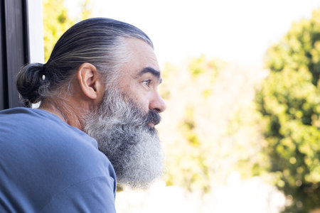 Senior man with beard looking out window, enjoying peaceful moment, copy space. elderly, contemplation, relaxation, tranquility, solitude, reflectionの写真素材