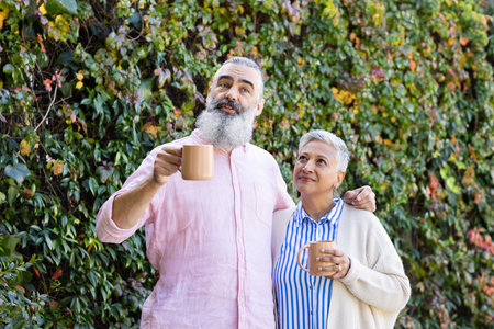 Enjoying coffee together, senior couple standing outdoors and smiling. Seniors, lifestyle,...