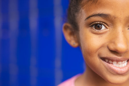 In school, young biracial girl with a bright smile is looking happy with copy space. She has brown eyes, light brown skin, and her hair pulled back, unaltered.の写真素材