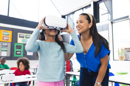 A middle-aged Asian woman assists young girl with a VR headset. Two biracial boys and African American boy study in background, unalteredの写真素材