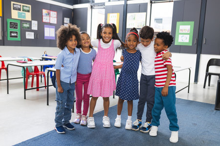 In school, six young students hugging, smiling in classroom. Diverse group wearing casual clothes,...
