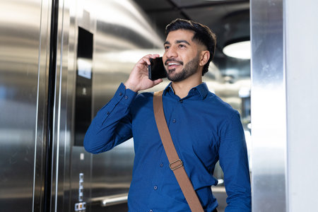 Talking on smartphone, businessman in blue shirt smiling in elevator. communication, professional,...