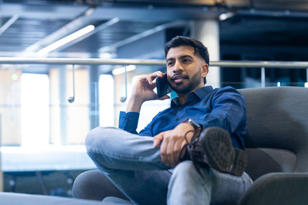 Talking on smartphone, man in casual attire sitting in modern office. Business, communication,...