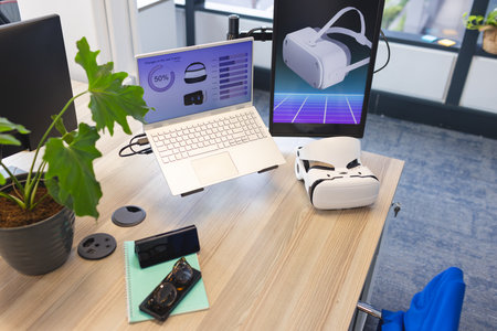 Desk with laptop displaying graphs and VR tech in contemporary business office. Various gadgets...