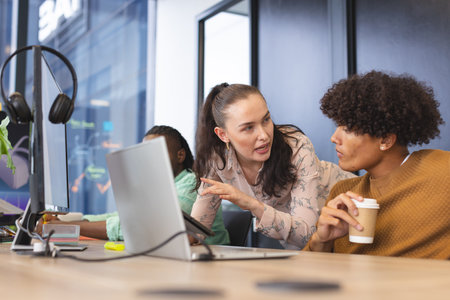 Diverse colleagues discussing over computer in office. The African American man wearing headphones,...