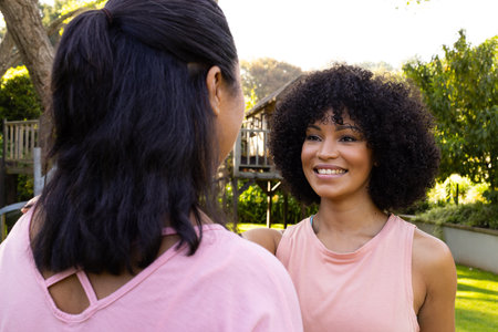 Biracial mother and daughter are talking outside at home. Both have curly hair, younger with light brown eyes, the older with dark, unalteredの写真素材