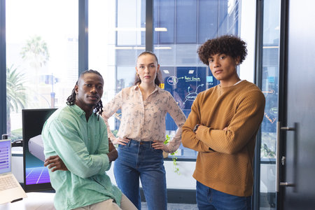 Diverse team standing in office, looking at camera. African American man wearing green shirt,...