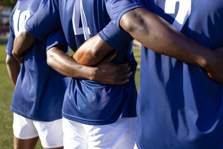 Three African American young male athletes, on field, wearing blue jerseys holding a rugby ball. They have dark skin and are fit, showcasing teamwork.の写真素材