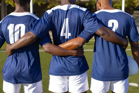 Three African American young male athletes standing together on field outdoors. They are wearing blue jerseys and have their arms crossed.の写真素材