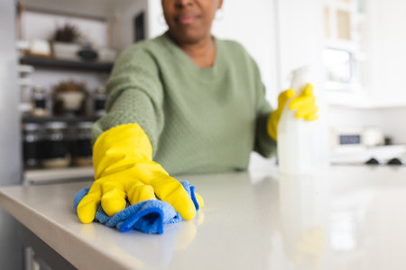 Happy senior african american woman wiping table in kitchen at home. Domestic life, retirement, cleaning and lifestyle, unaltered.の写真素材