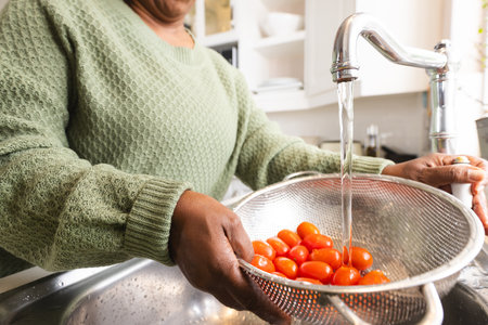 Senior african american woman washing tomatoes in kitchen at home. Domestic life, retirement, food and lifestyle, unaltered.の写真素材