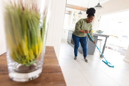 Happy senior african american woman cleaning floor with mop at home. Domestic life, retirement,...