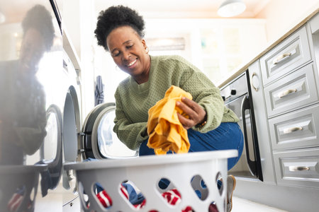 Happy senior african american woman doing laundry in kitchen at home. Domestic life, retirement, cleaning and lifestyle, unaltered.の写真素材