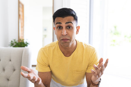 Middle Eastern man gestures in confusion during a video call at home, with copy space. His expression suggests a candid moment of uncertainty or surprise.の写真素材