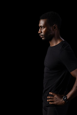 African American man in a contemplative pose, with copy space on a black background. His profile is accentuated against a dark background, evoking introspection.の写真素材