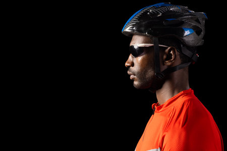 African American man in cycling gear poses confidently on black background, with copy space. Profile...