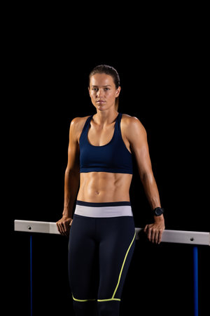 Young Caucasian female athlete stands confidently at the gym on a black background, overcoming...