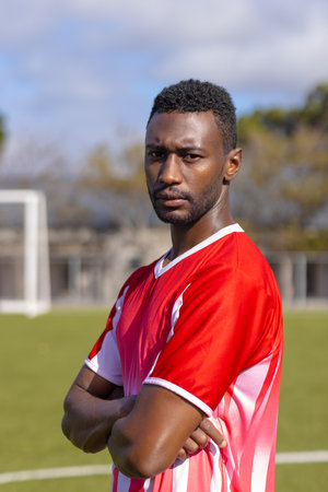African American young male athlete standing on soccer field outdoors, looking serious, copy space. Wearing red and white jersey, short black hair, focused eyes, unalteredの写真素材