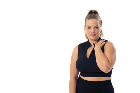 Plus size Caucasian young female model in black sportswear on white background, copy space. She has blonde hair, blue eyes, and is touching her shoulder, embodying body positivity, unalteredの写真素材