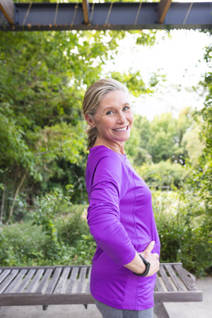 Outdoors, senior Caucasian female standing, smiling, hands on hips. Light-skinned with wrinkles,...