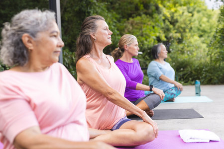 Diverse senior female friends practicing yoga outdoors. Wearing casual sportswear, concentrating, enjoying together under blue background, unalteredの写真素材