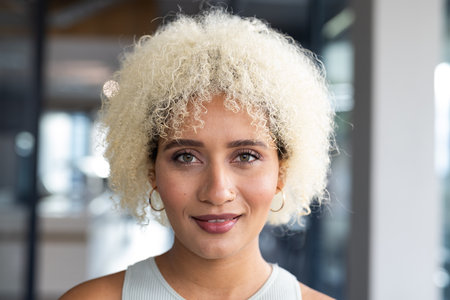 In modern office, young biracial female with curly blonde hair smiling. Wearing light makeup and...