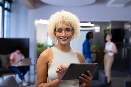 In modern office, a diverse young team with a biracial woman holding a tablet. With curly blonde...