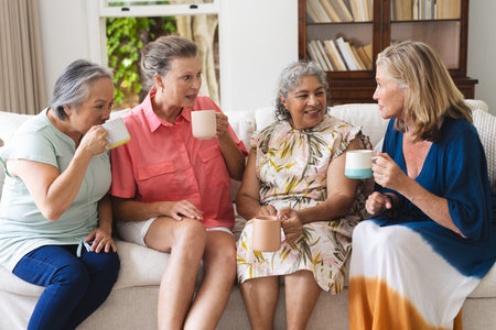 Diverse senior female friends enjoying coffee together at home. Displaying mix of Asian and...