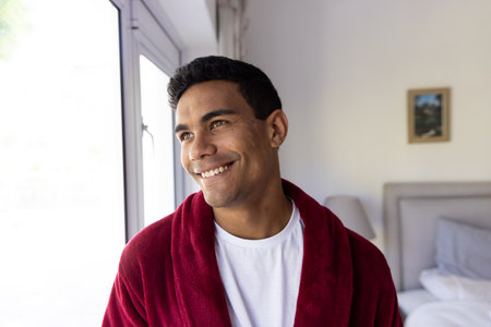 Young biracial man smiles warmly at home, with copy space. He exudes a sense of comfort and relaxation in a cozy indoor setting unaltered.の写真素材