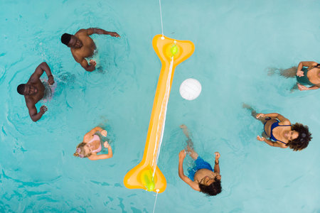 Overhead of happy diverse friends playing fun game of volleyball in sunny swimming pool, copy space....