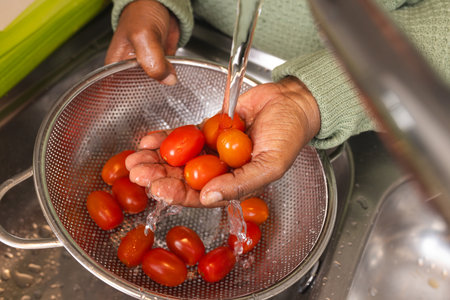 Senior african american woman washing tomatoes in kitchen at home. Domestic life, retirement, food...