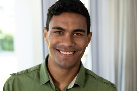 Young biracial man smiles warmly, with copy space. His cheerful expression adds a welcoming...