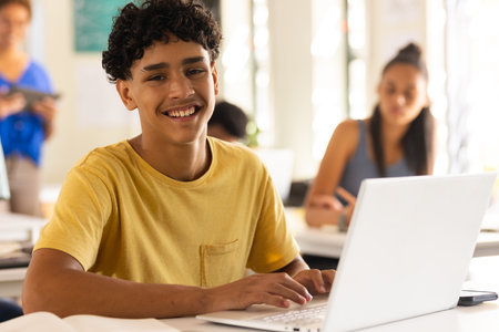 Smiling teenage boy using laptop in high school classroom, engaging in learning activities. Education, student, technology, studying, academic, digitalの写真素材