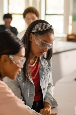 In high school, teenage girls wearing safety goggles working on science experiment. Education,...
