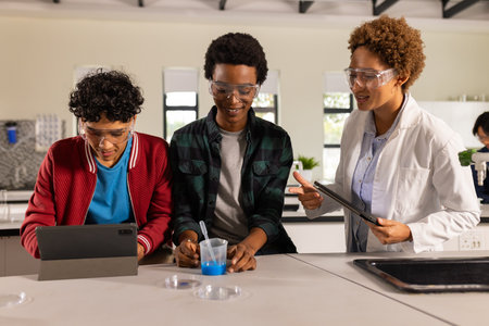 Conducting science experiment with tablet and beaker, teenagers in high school classroom. Education, chemistry, technology, students, learning, laboratoryの写真素材