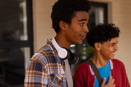 Teenage boys smiling and talking outside high school building, wearing casual clothes. Teenagers,...
