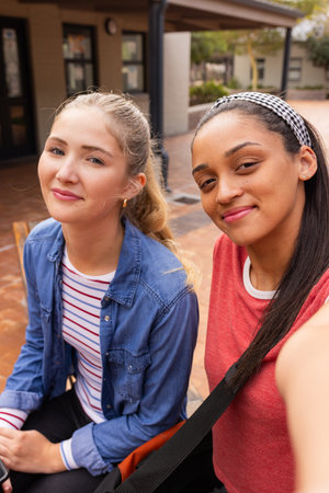 Smiling teenage girls sitting together outside high school, enjoying their break. Friendship,...