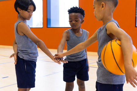 "In school gym, boys in sportswear huddling with basketball, preparing for game. teamwork, training, gymnasium, huddle, energy, competitionの写真素材