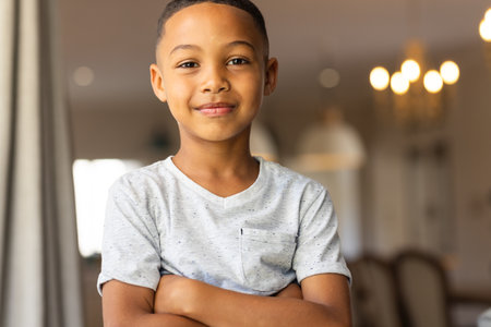 "Smiling boy standing with arms crossed in living room, feeling confident. Confidence, child, home, happiness, self-assured, portraitの写真素材