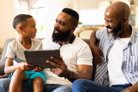 "Using tablet, father and son sitting on couch with grandfather smiling. Family, generation, bonding, technology, happiness, connectionの写真素材