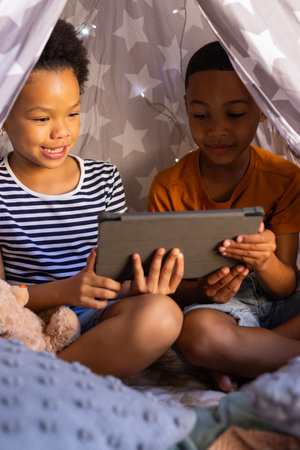 "brother and sister sitting in blanket fort, watching tablet together, enjoying screen time, in teepee. Family, bonding, childhood, indoors, imagination, technology, in teepeeの写真素材
