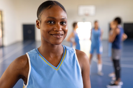 Smiling female basketball player in uniform standing on court with teammates. Sports, teamwork,...