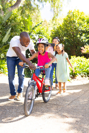 Father teaching daughter to ride bicycle, family enjoying outdoor activity together. bonding,...