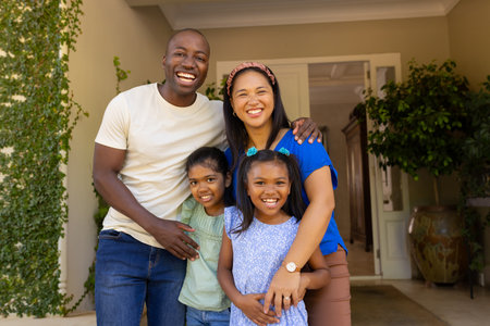 Smiling family of four with daughters standing together outside home, enjoying quality time. togetherness, bonding, happiness, outdoors, lifestyle, parenthoodの写真素材