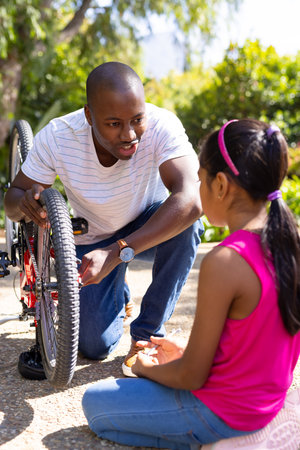 Fixing bicycle, father teaching daughter how to repair bike outdoors. fatherhood, mechanics, family,...