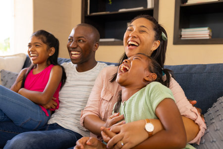 Laughing together, happy family of four sitting on couch at home. togetherness, happiness, bonding, living room, parenting, joyの写真素材